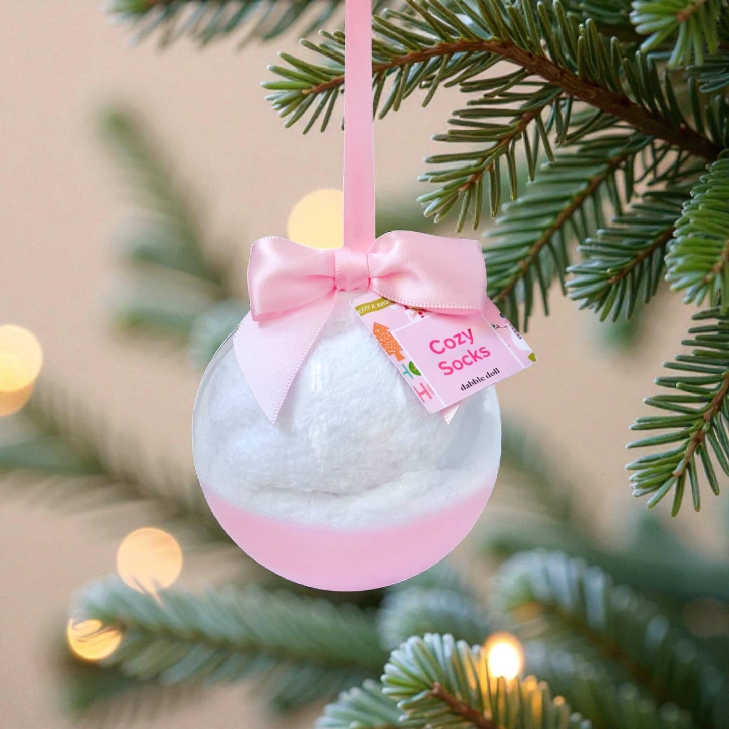 Dabble Doll Cozy Socks ornament with pink bow hanging on a Christmas tree branch