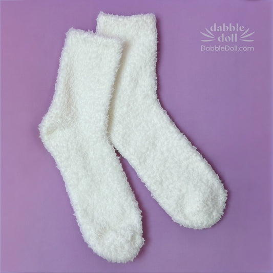 Pair of white fuzzy socks on a purple background with 'Dabble Doll' branding.