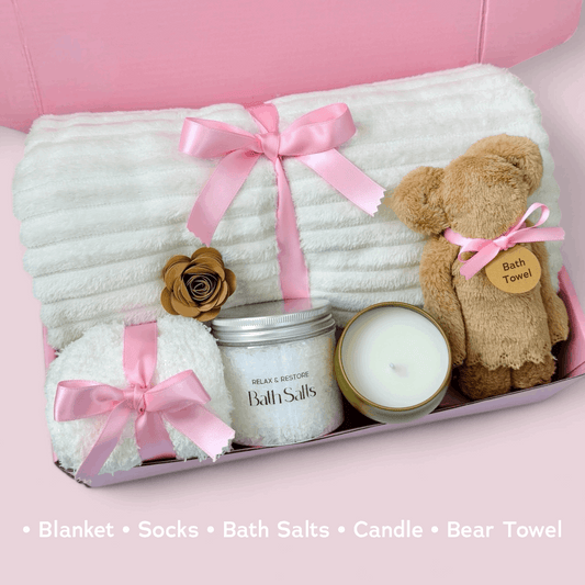 Dabble Doll care package with blanket, socks, bath salts, candle, and bear towel in a pink gift box