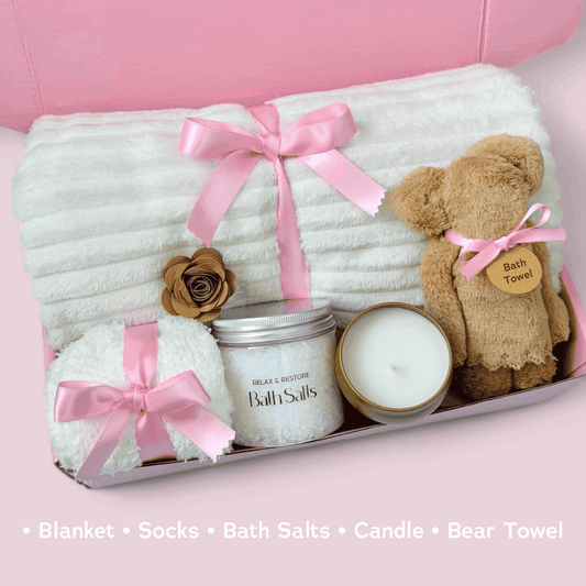 Dabble Doll care package with blanket, socks, bath salts, candle, and bear towel in a pink gift box