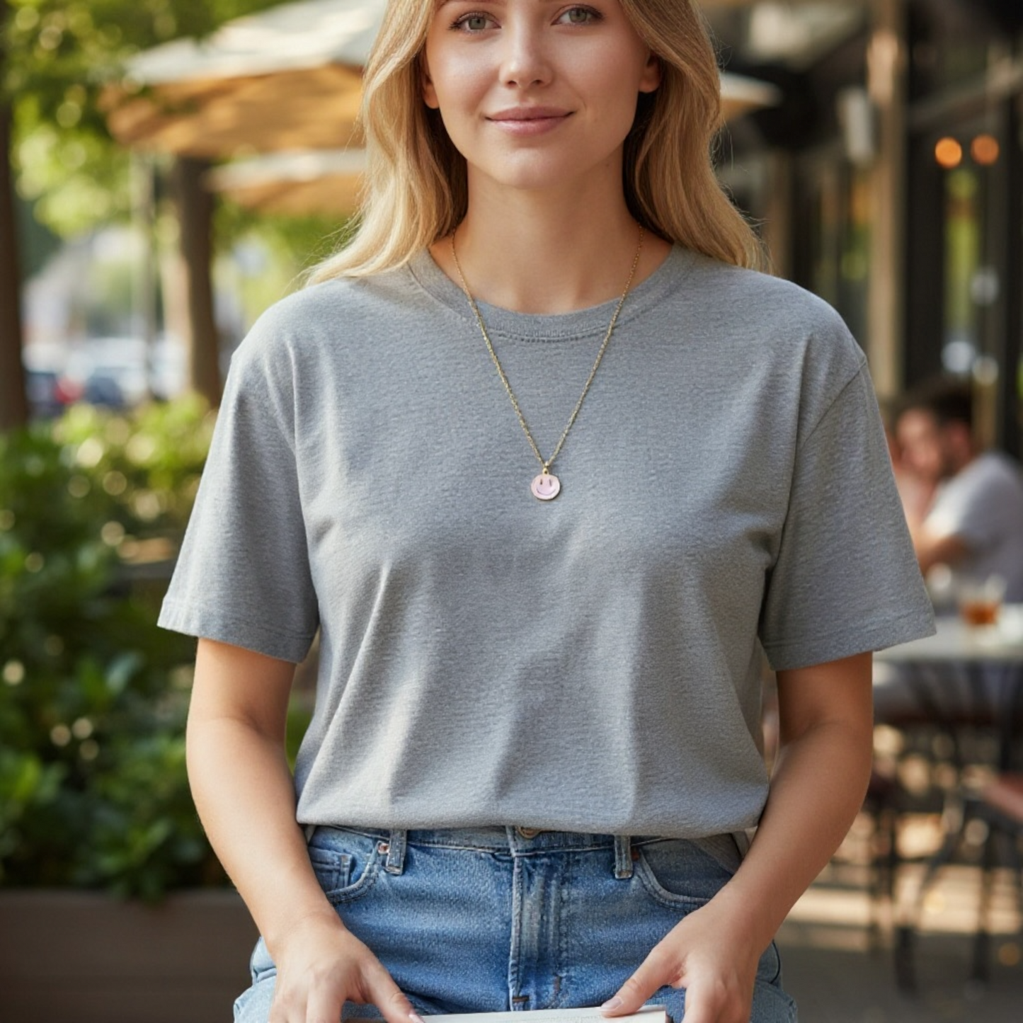 Casual woman wearing a light gray t-shirt with a charm and necklace in an outdoor café setting