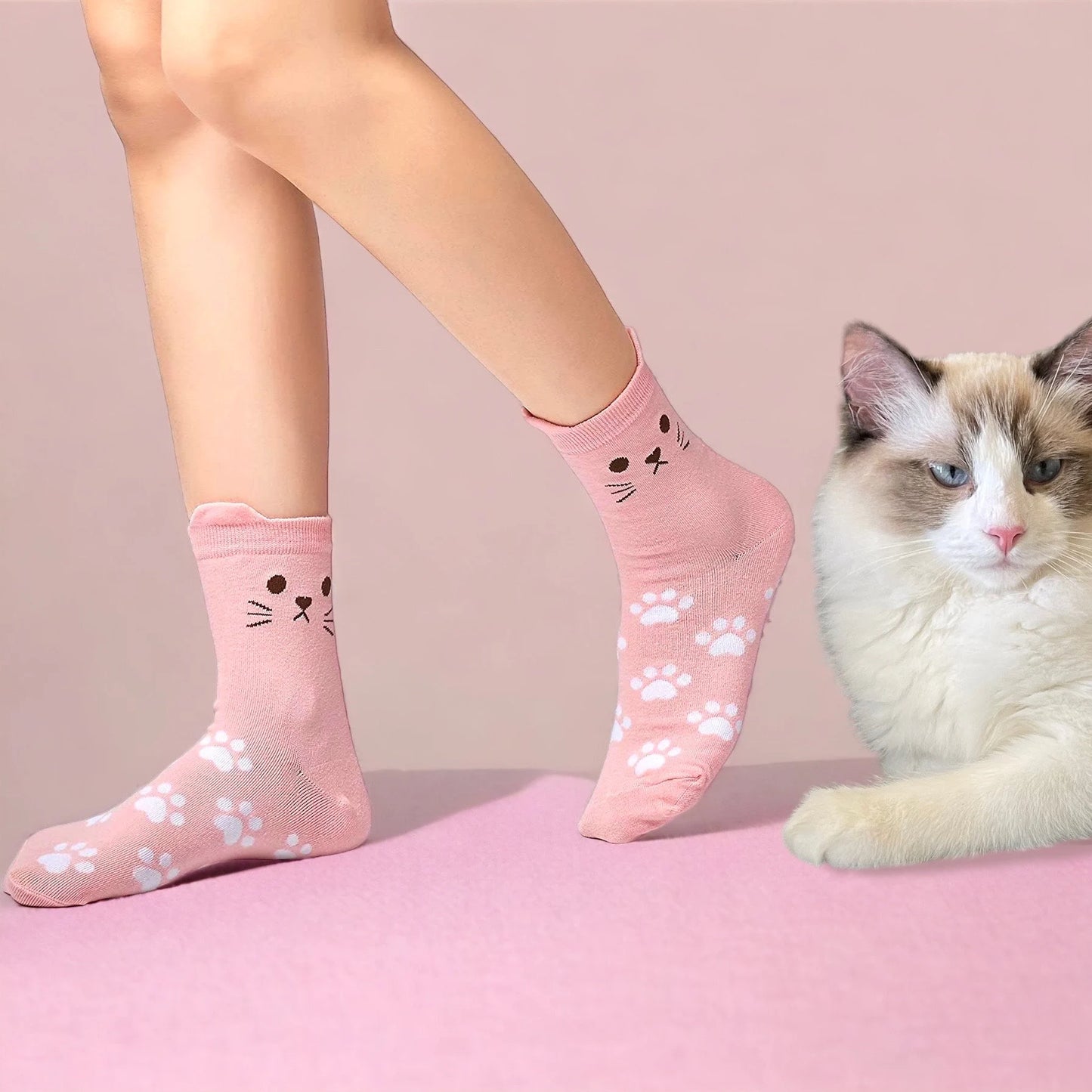 Cute pink cat socks with paw prints worn on feet next to a fluffy white and gray cat