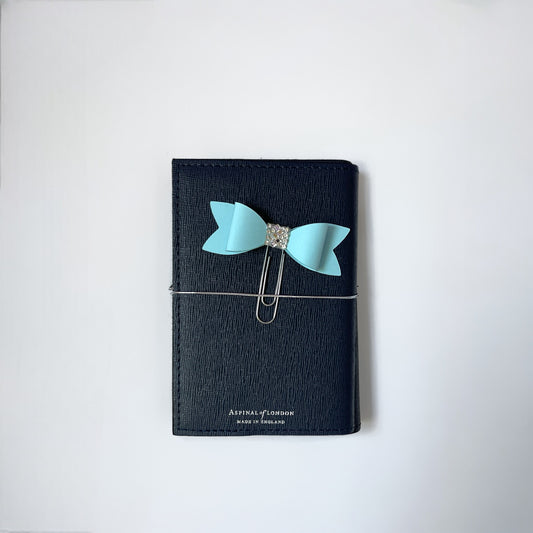 Dabble Doll Bow paperclip in light blue attached to a black notebook for stylish organization