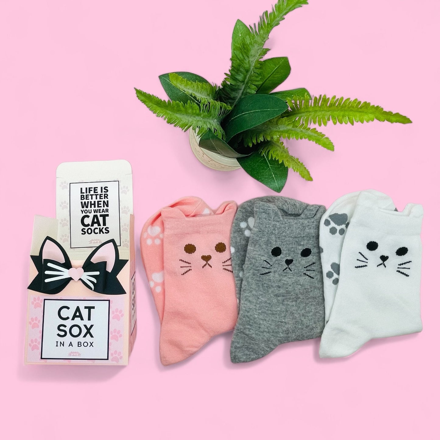 Dabble Doll cat socks gift box with three pairs of pink gray and white cat face socks on pink background