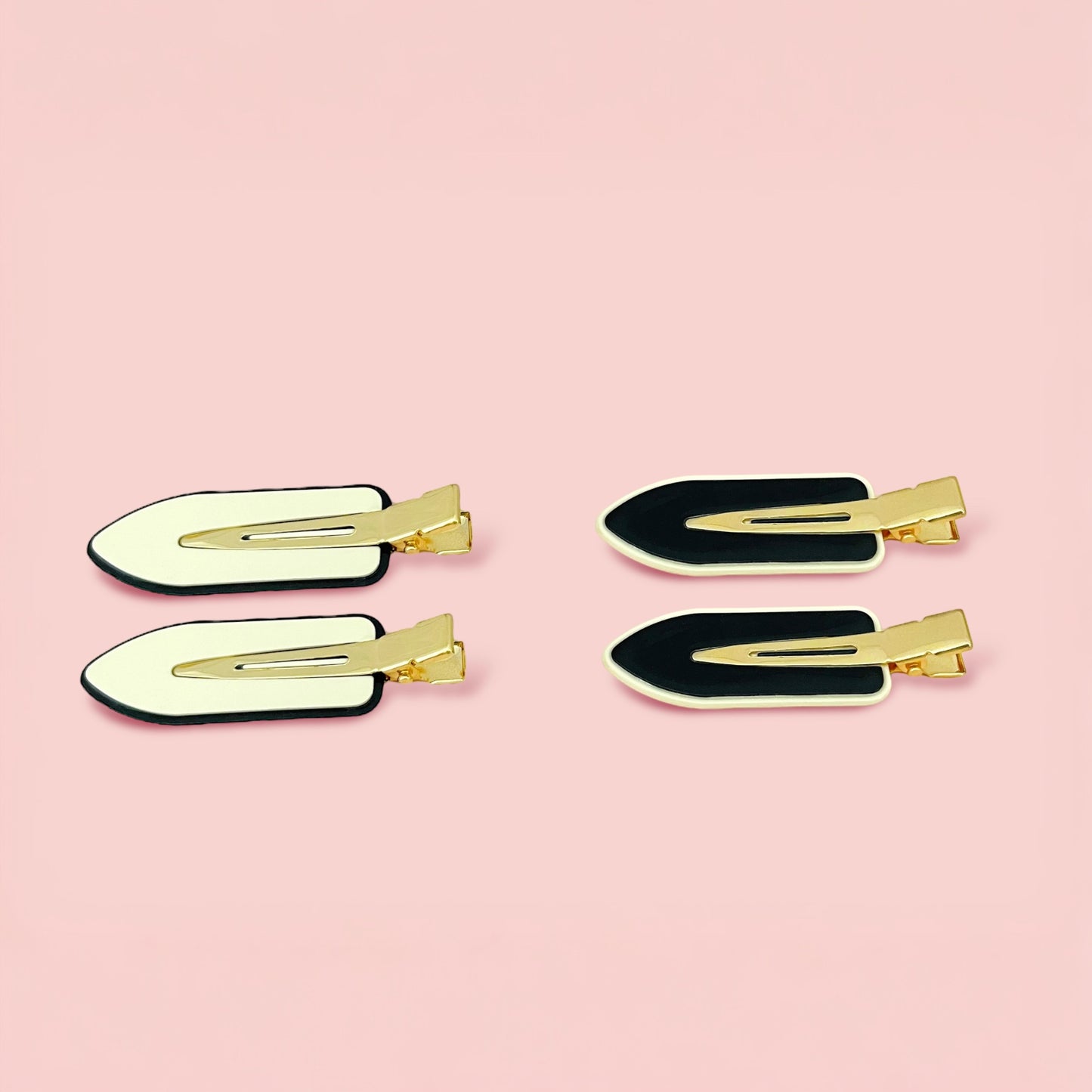Set of four Dabble Doll creaseless hair clips in black and white with gold clasps on pink background
