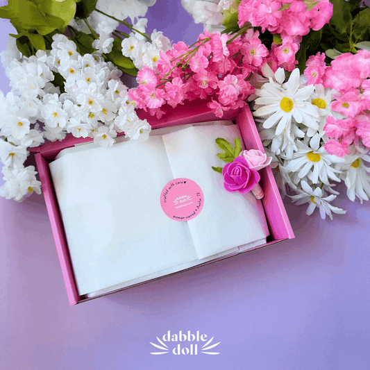 Dabble Doll pink relaxation care package gift box surrounded by pink and white flowers