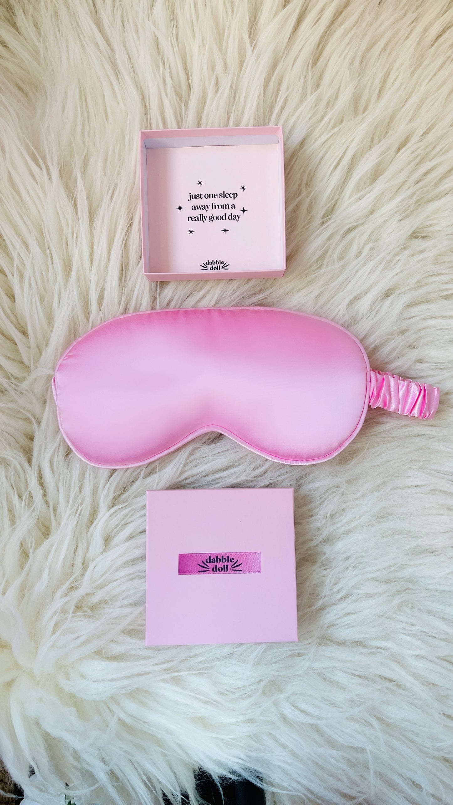Pink silky sleep mask gift box set from Dabble Doll with soft fabric and elastic band on white fur background