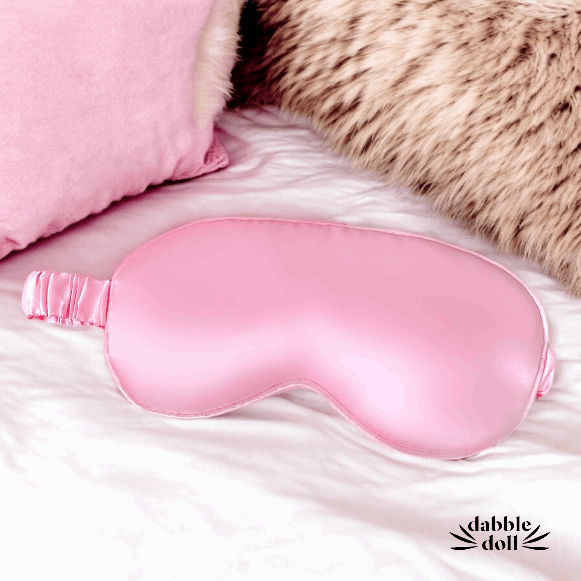 Pink satin sleep mask from the pink spa gift box for her by Dabble Doll on a soft bed