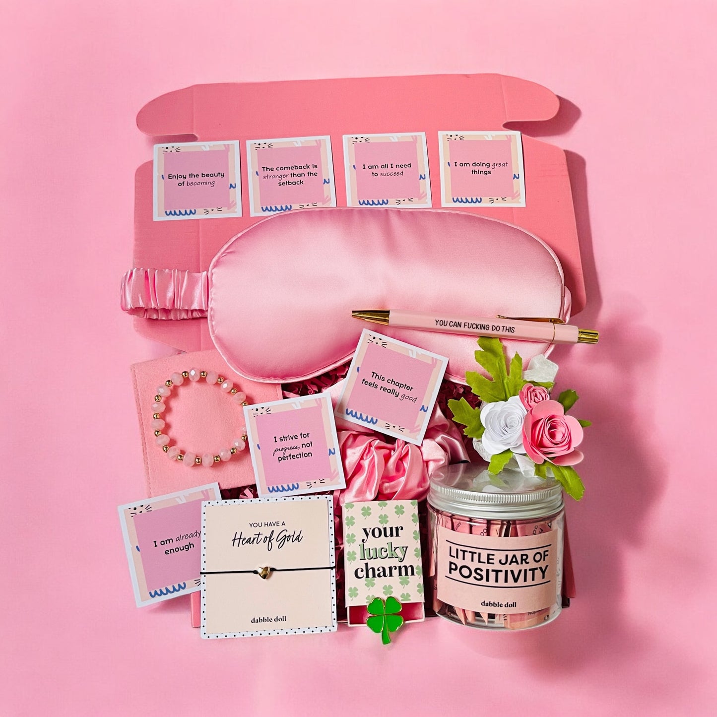 Dabble Doll positivity care package gift box with pink eye mask, bracelet, jar of positivity, and inspirational cards