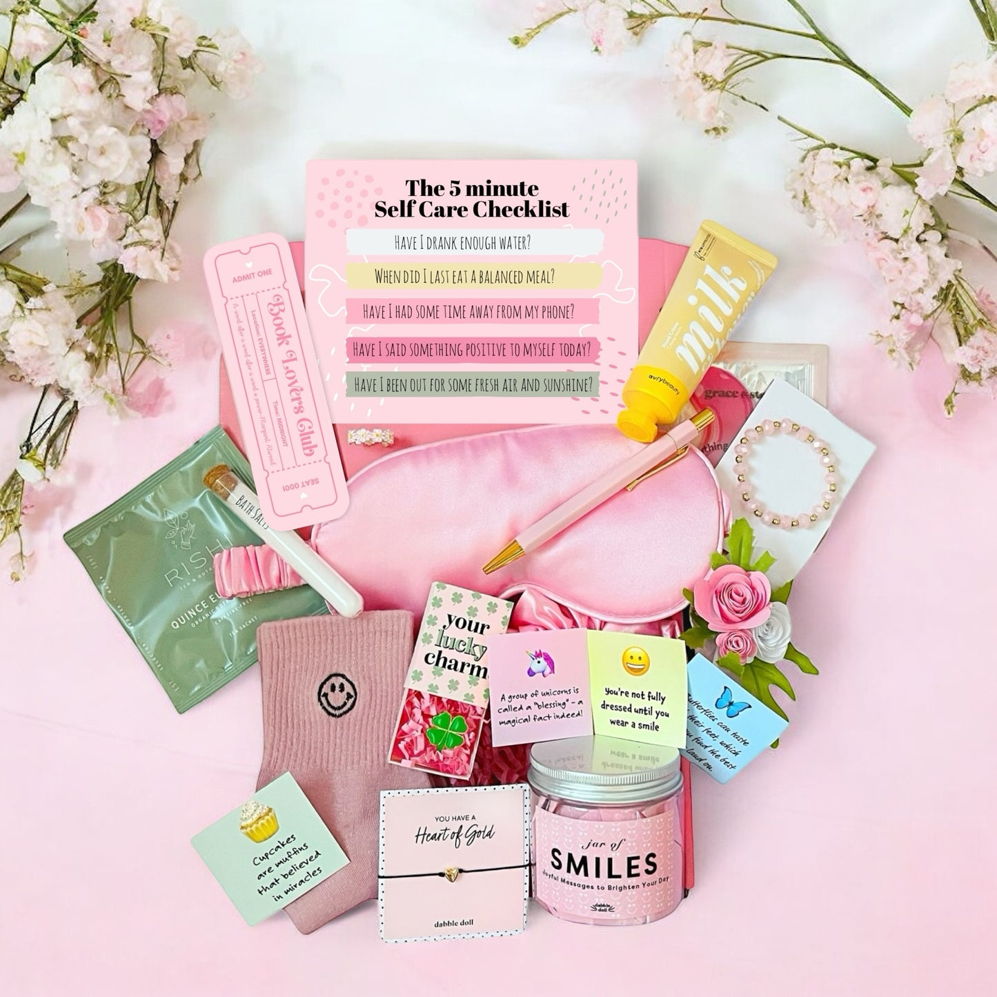 Dabble Doll self-care gift box for women including skincare items, socks, checklist, and accessories on pink background