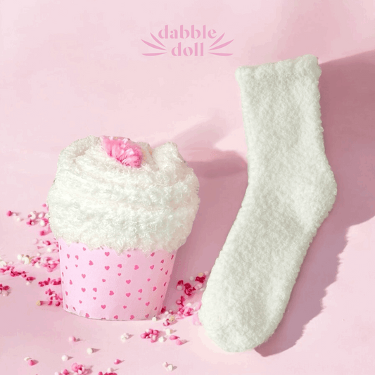 Dabble Doll thinking of you care package for women featuring cozy white socks and soft heart-patterned packaging