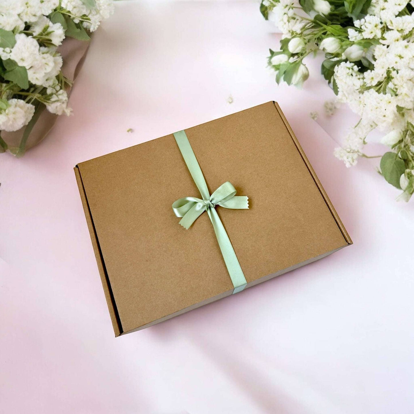 Dabble Doll hygge gift box with green ribbon bow on brown cardboard surrounded by white flowers