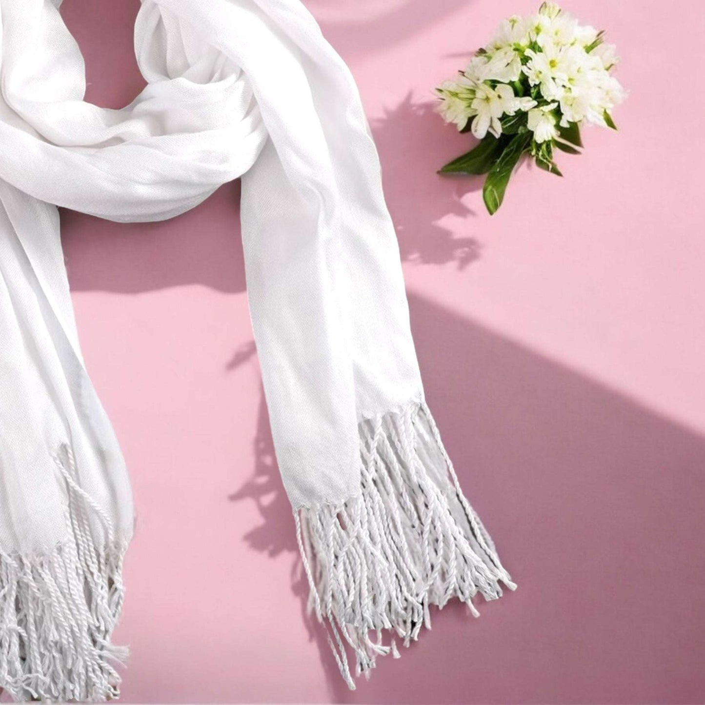 Romantic gift box for wife featuring a soft white scarf with fringes and a small bouquet of white flowers on pink background
