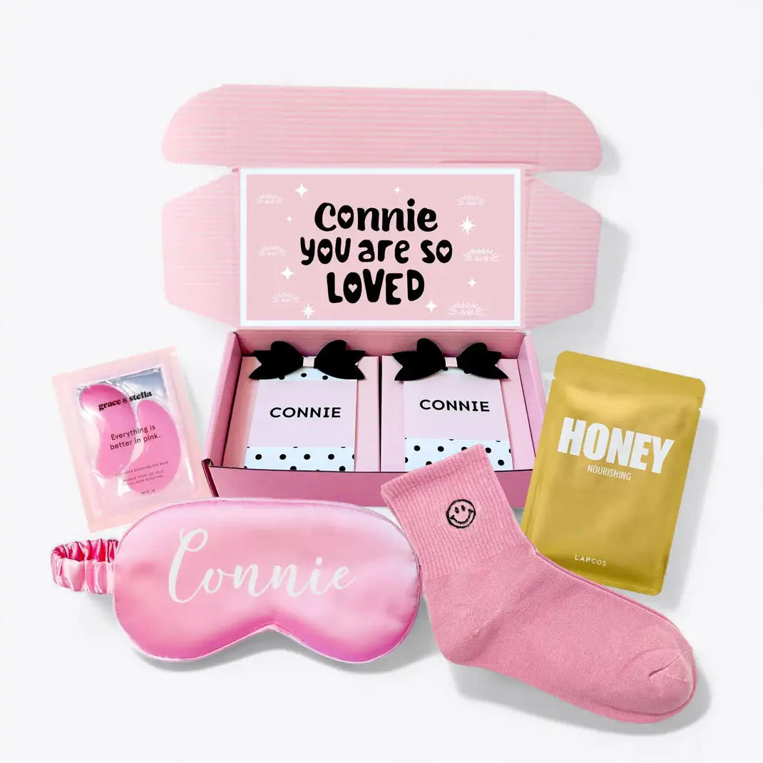 Unique gift hampers for her featuring personalized sleep mask, cozy socks, honey pouch, and skincare items in a pink box
