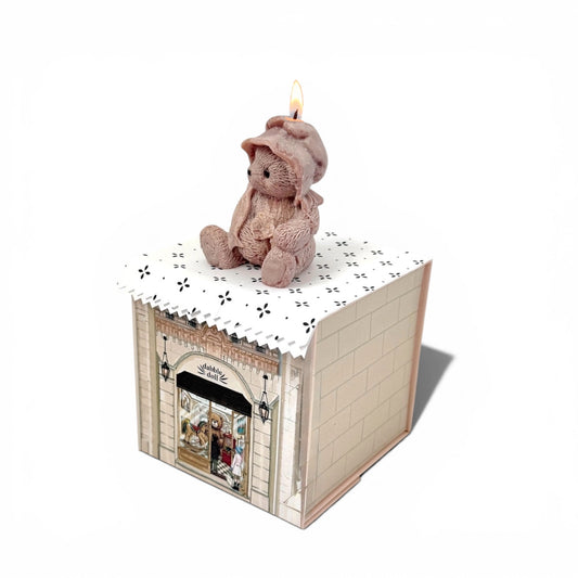 Teddy bear on a small table with a candle inside a decorative box on a white background