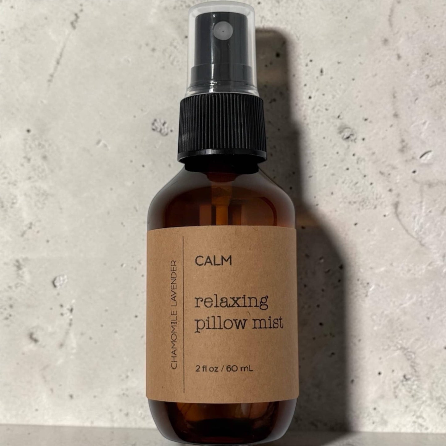 Brown spray bottle labeled 'Calm Relaxing Pillow Mist' on a textured gray background