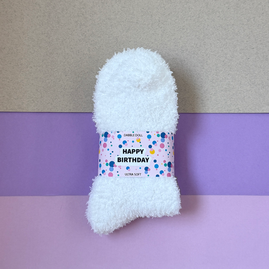 White fluffy sock with a 'Happy Birthday' label on a purple and gray background