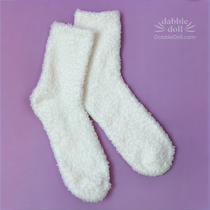 Pair of white fuzzy socks on a purple background with 'Dabble Doll' branding.
