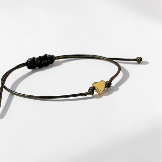 Black cord bracelet with a gold heart charm on a white background