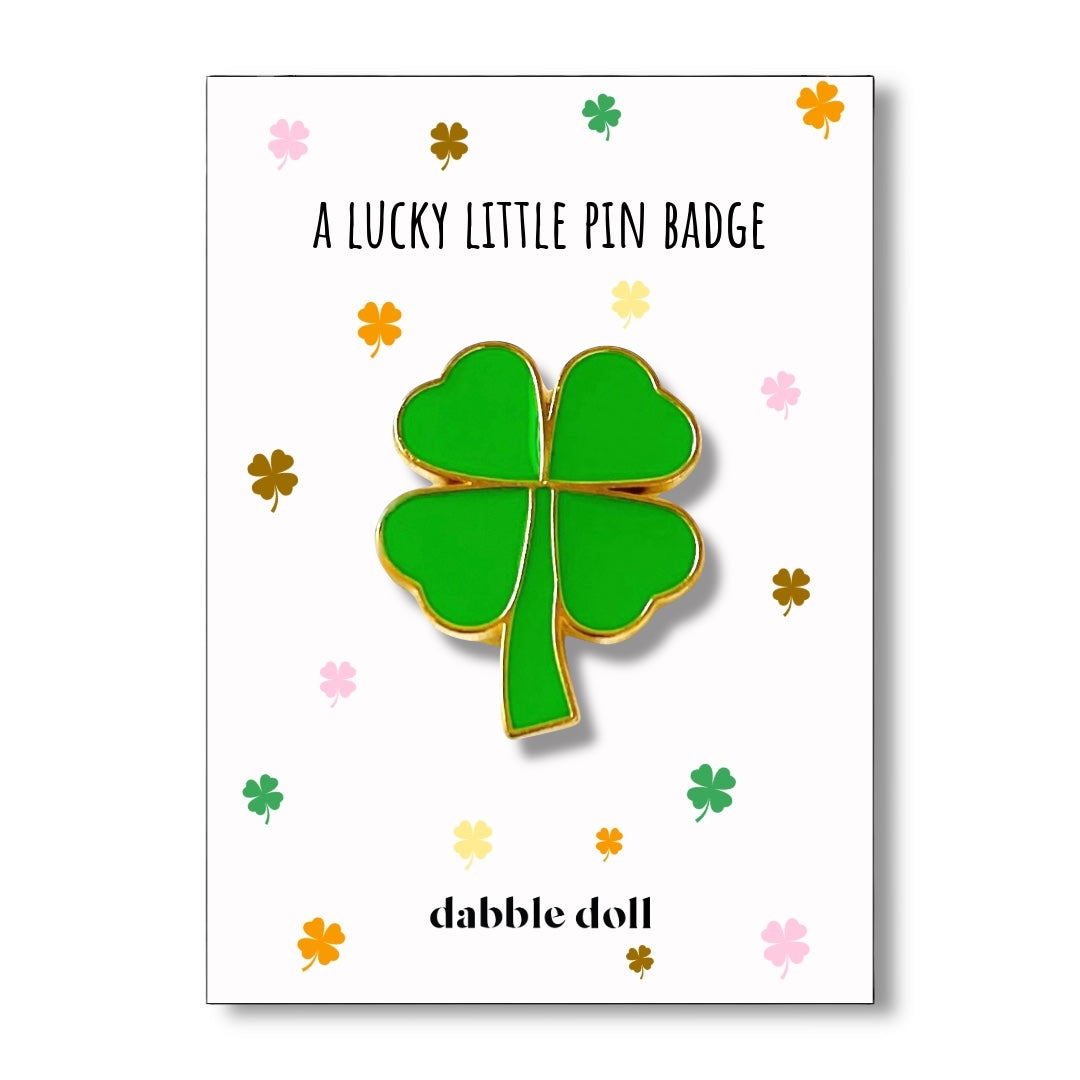 Green four-leaf clover pin badge on a white card with 'dabble doll' branding