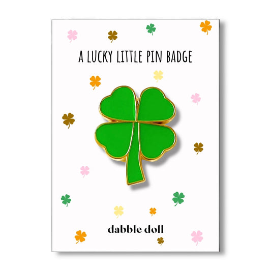 Green four-leaf clover pin badge on a white card with 'dabble doll' branding
