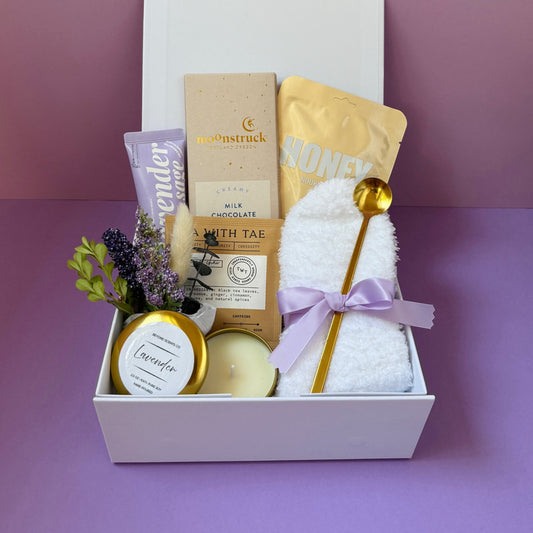 Gift basket with lavender candle, chocolate bar, honey, towel, and spoon on a purple background