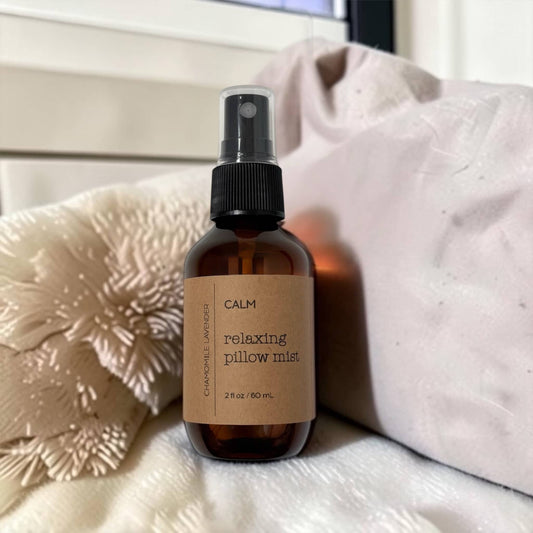Brown spray bottle labeled 'Calm Relaxing Pillow Mist' on a textured surface with pillows in the background.