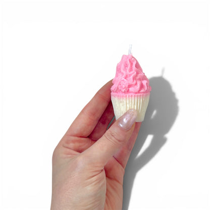 Hand holding a cupcake-shaped candle with pink frosting against a white background