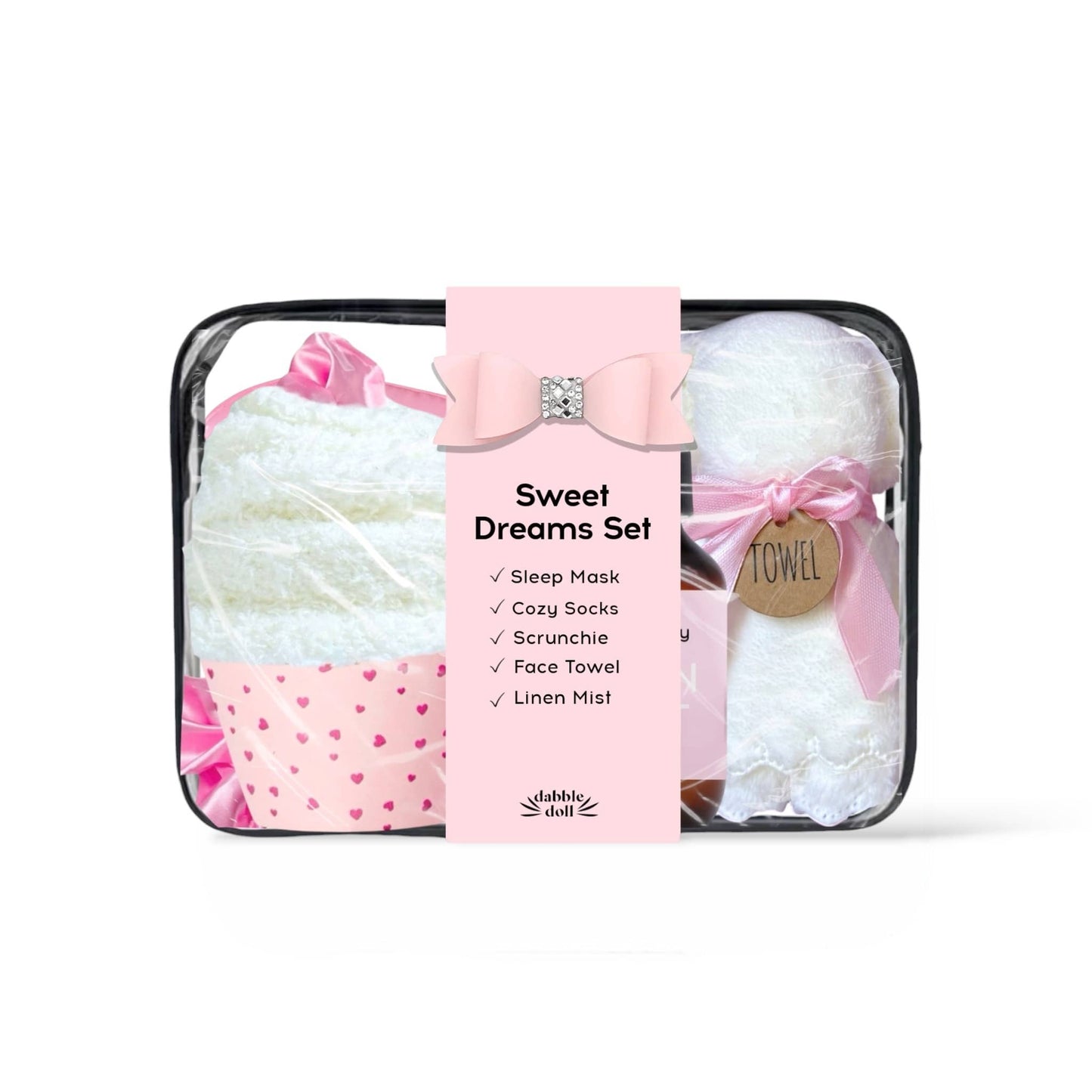 Sweet Dreams Set by Bubble Shell in a clear zippered bag with a pink paper label. The set includes a white sleep mask with a pink bow, white cozy socks with a pink heart pattern, a white face towel, and white linen mist tied with a pink ribbon.
