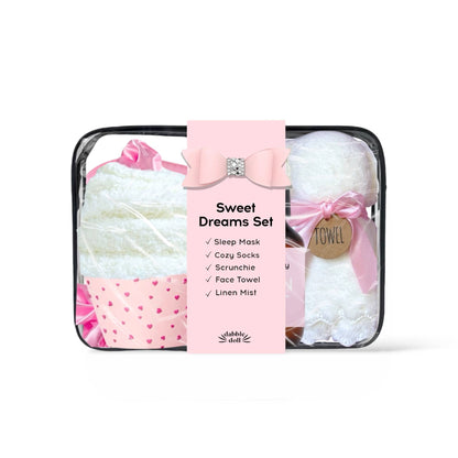 Sweet Dreams Set by Bubble Shell in a clear zippered bag with a pink paper label. The set includes a white sleep mask with a pink bow, white cozy socks with a pink heart pattern, a white face towel, and white linen mist tied with a pink ribbon.