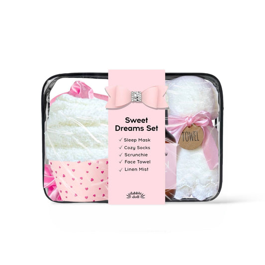 Sweet Dreams Set by Bubble Shell in a clear zippered bag with a pink paper label. The set includes a white sleep mask with a pink bow, white cozy socks with a pink heart pattern, a white face towel, and white linen mist tied with a pink ribbon.