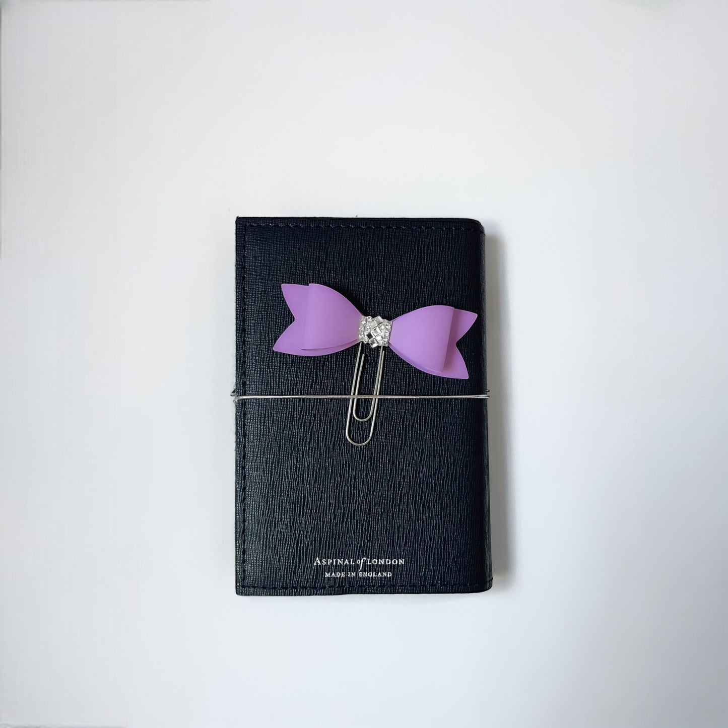 Dabble Doll Bow Paperclip in Purple attached to a sleek black notebook, perfect for organizing notes