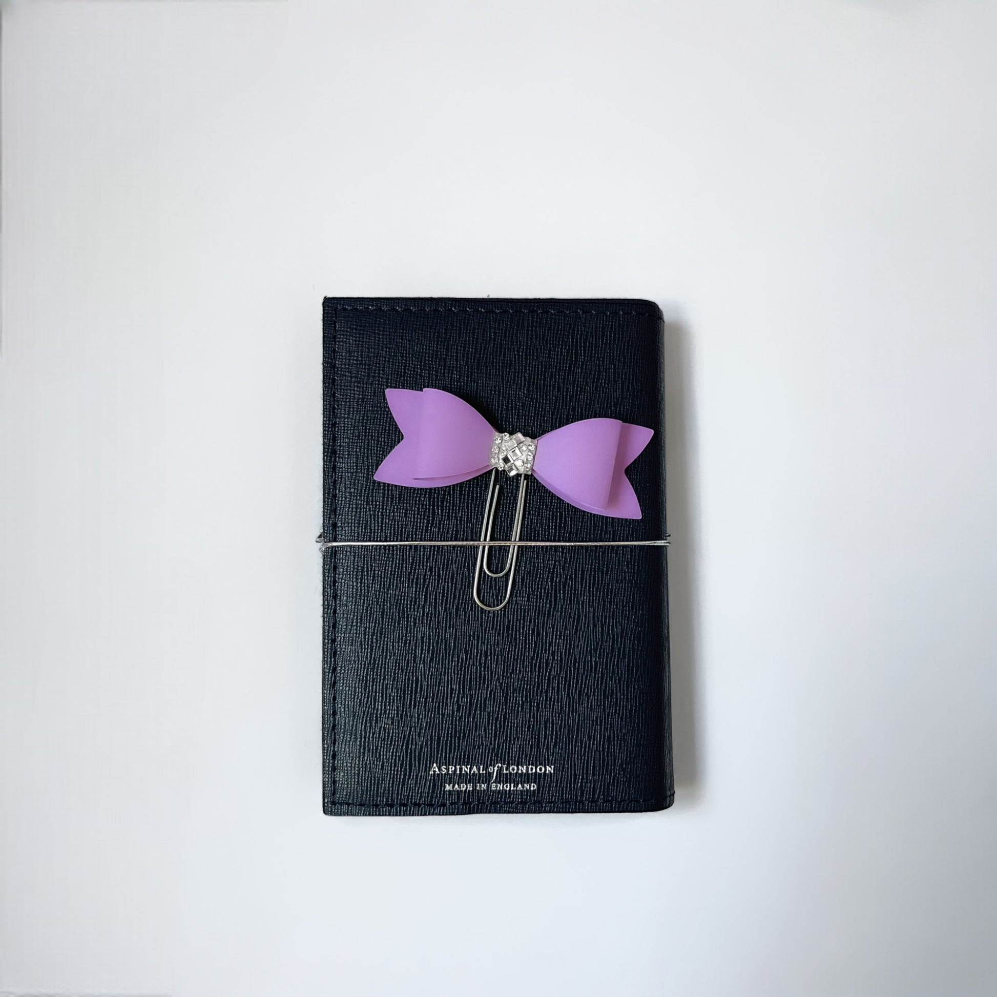 Dabble Doll Bow Paperclip in Purple attached to a sleek black notebook, perfect for organizing notes