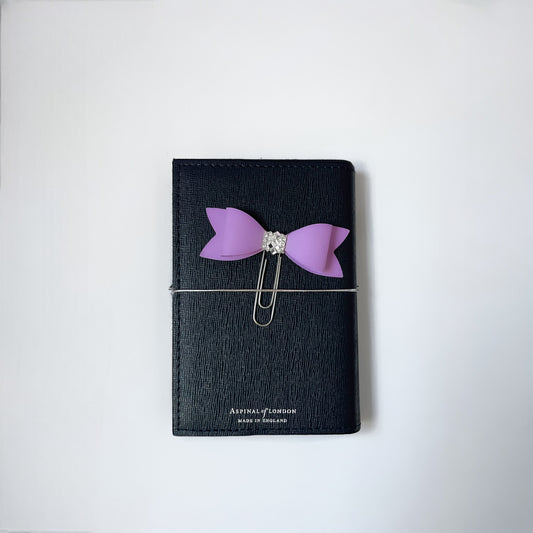 Dabble Doll Bow Paperclip in Purple attached to a sleek black notebook, perfect for organizing notes
