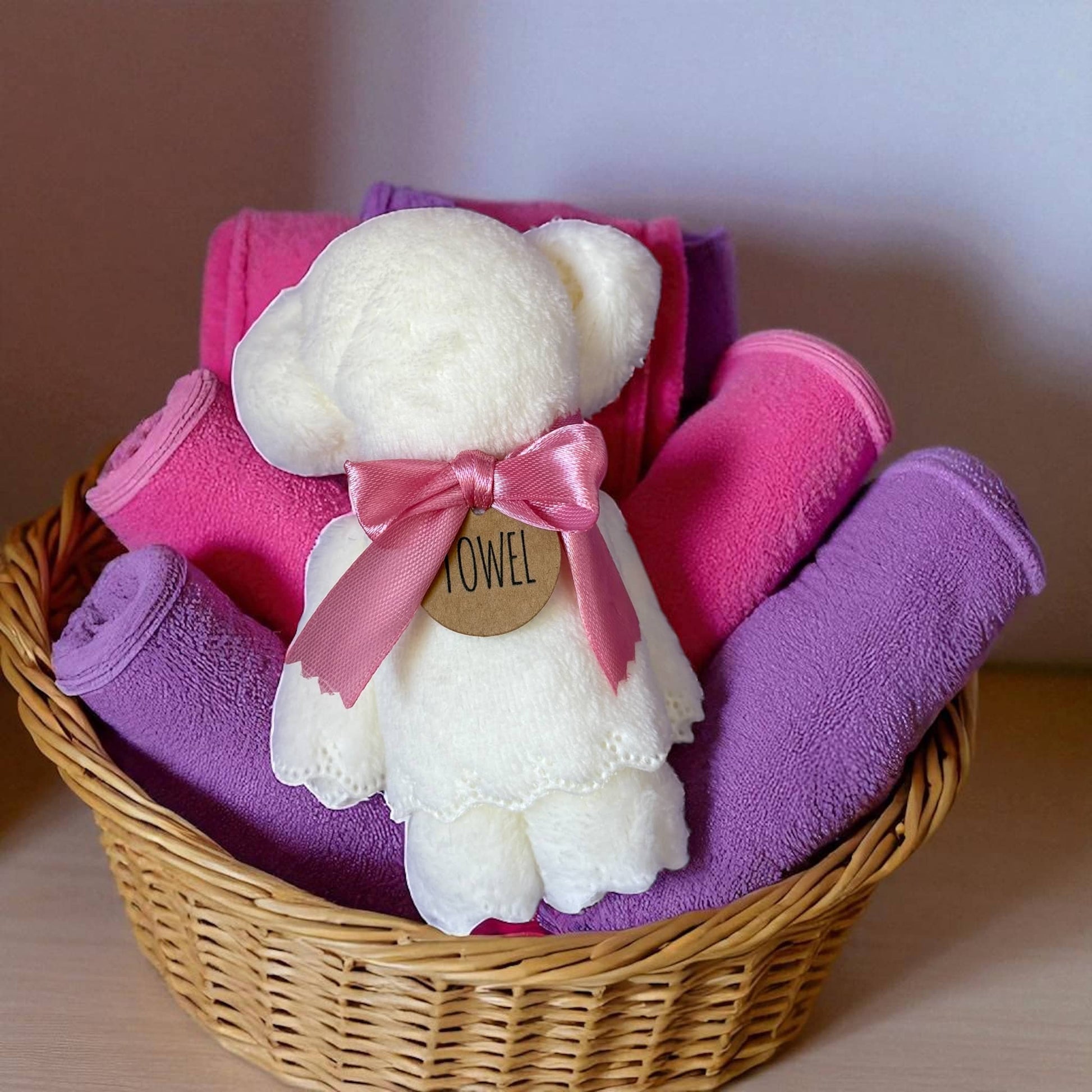 Dabble Doll bear towel with pink and purple towels in a wicker basket for children's bath time
