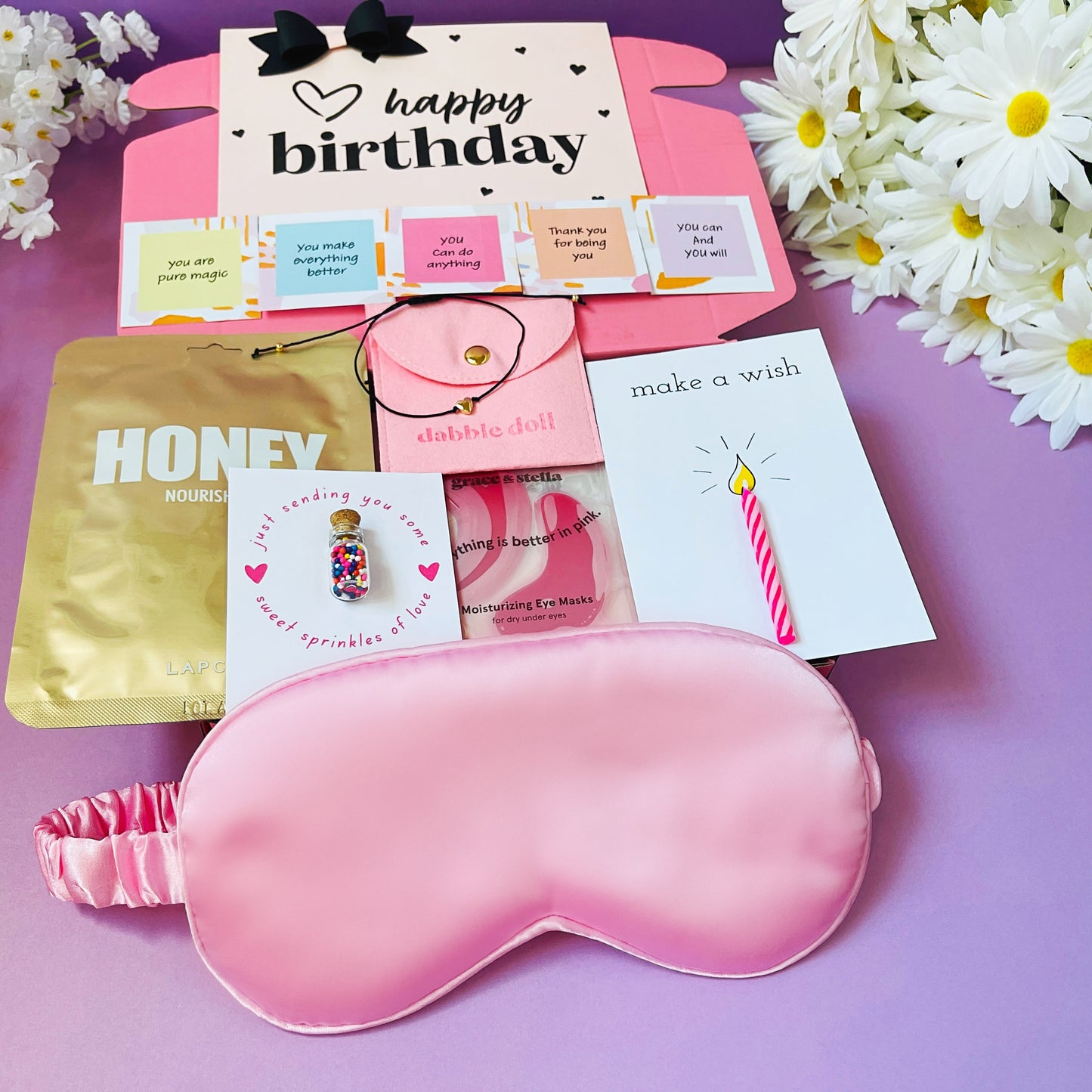 Dabble Doll birthday gift set with a pink sleep mask, cards, and honey nourishing masks for a special celebration