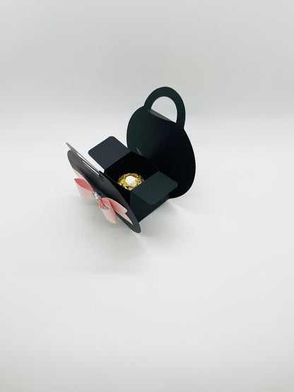 Dabble Doll black purse favor bags with pink bow and rhinestone detail, open showing a gold-wrapped candy inside