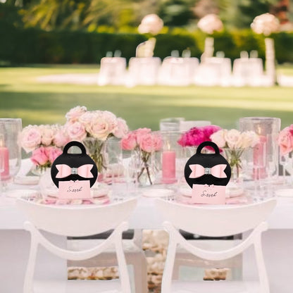 Elegant black purse favor bags with pink bows on a decorated outdoor party table