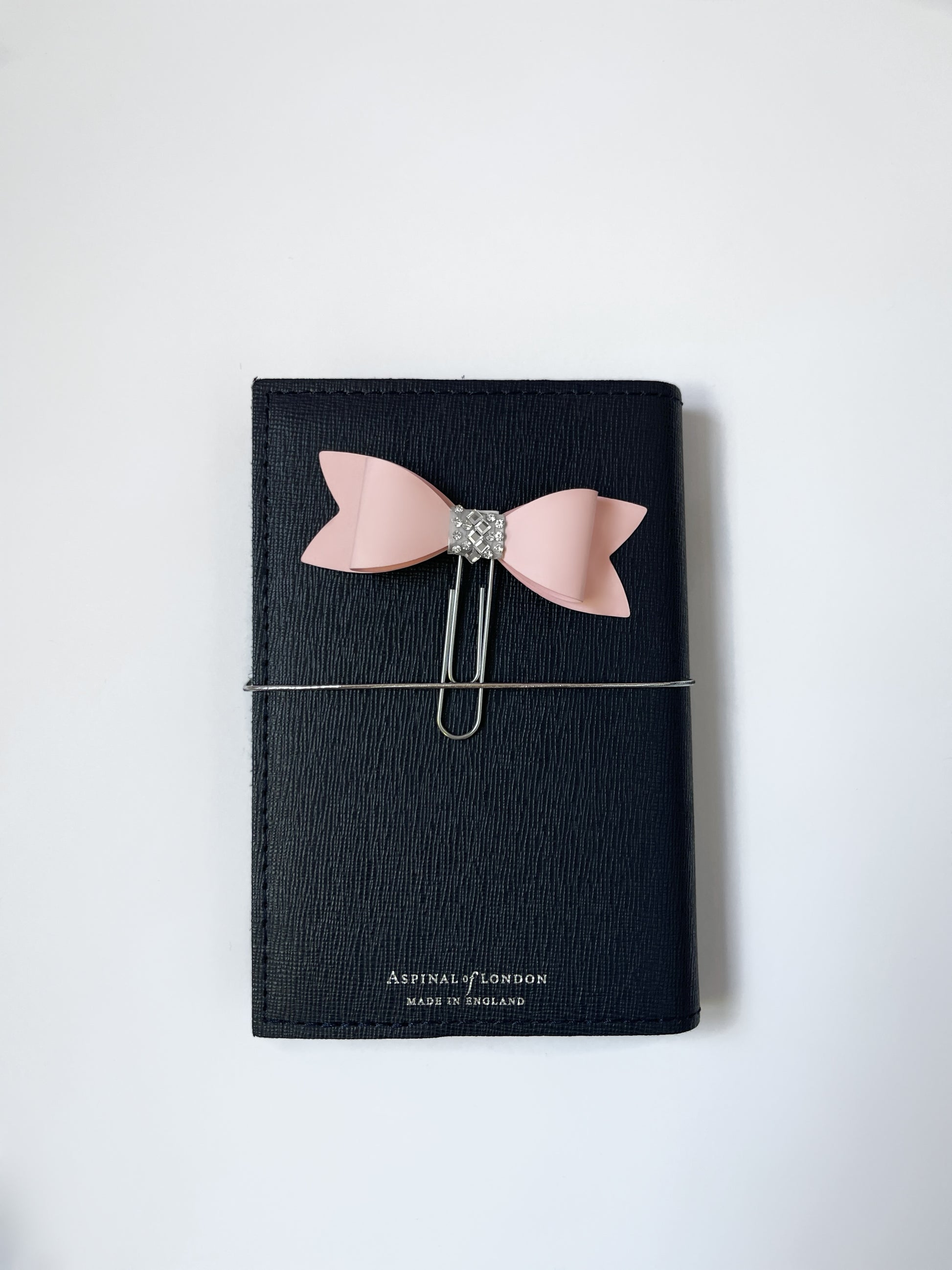 Dabble Doll pink bow bookmark attached to a black notebook for stylish organization