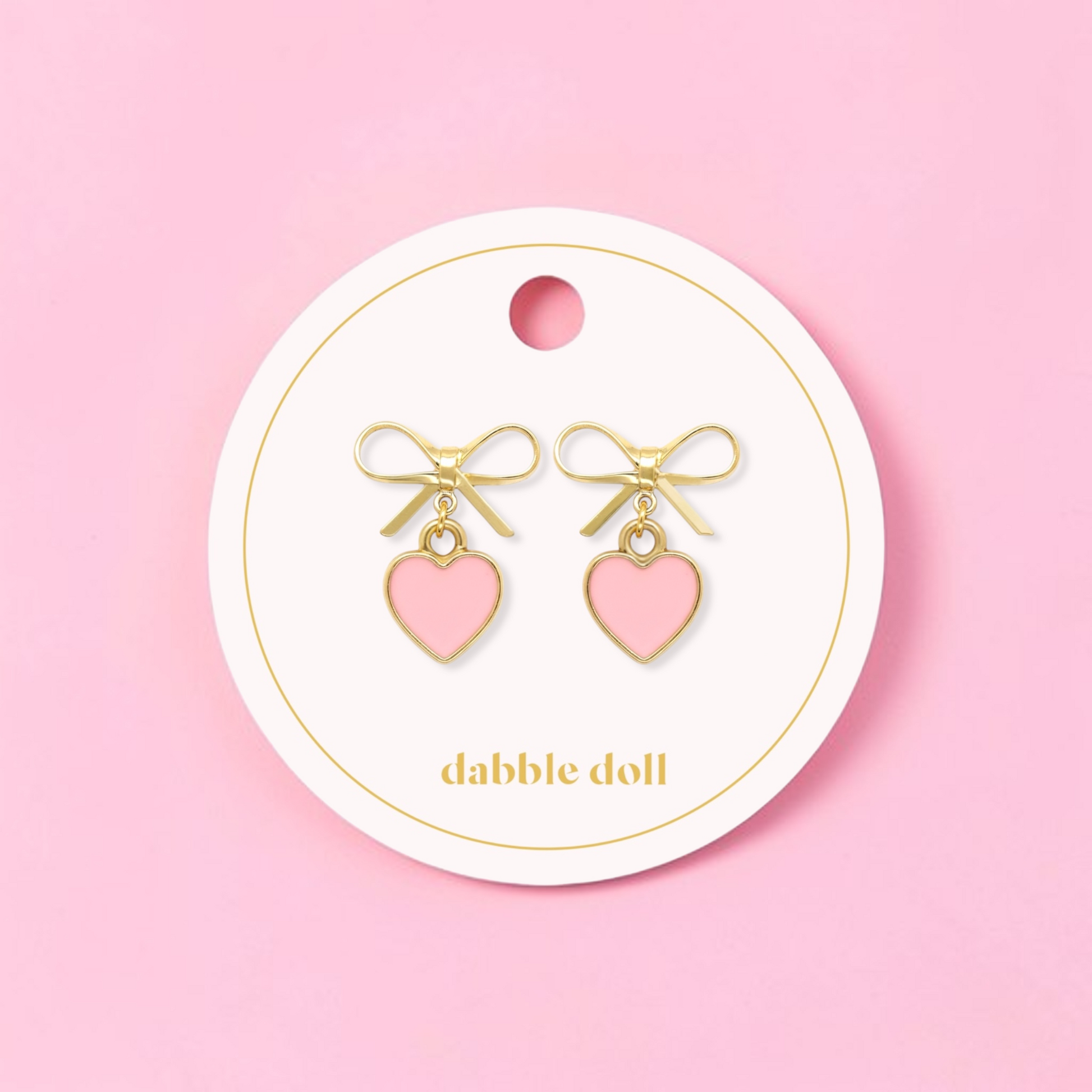 Dabble Doll bow earrings featuring gold accents and pink heart charms for a cute accessory look