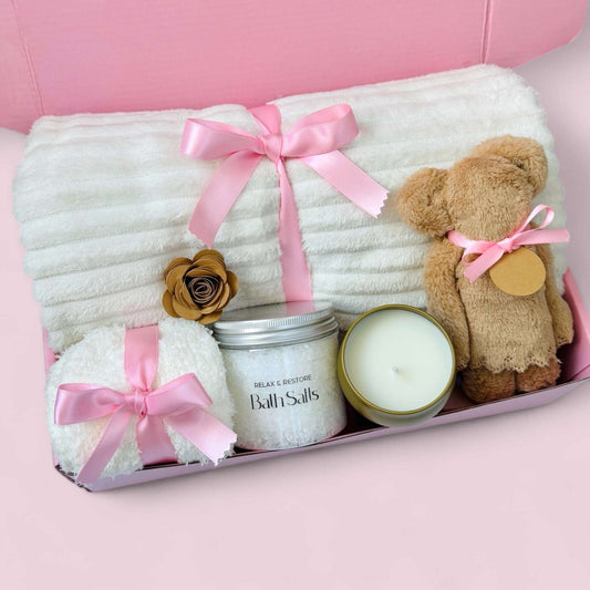 Dabble Doll care package gift box featuring a cozy blanket, teddy bear, bath salts, and a scented candle