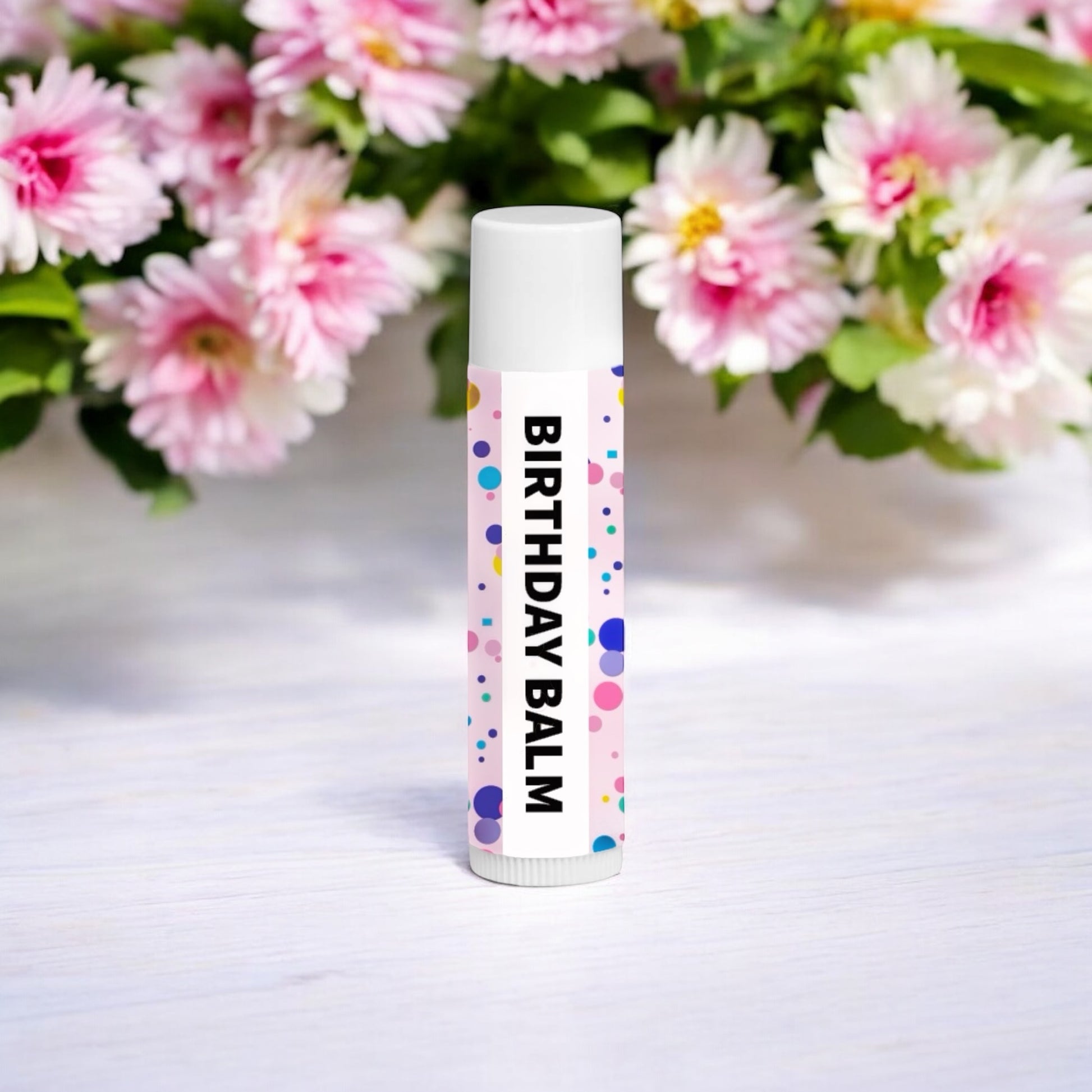 Dabble Doll Birthday Balm Chapped Lip Balm in a colorful tube with floral background