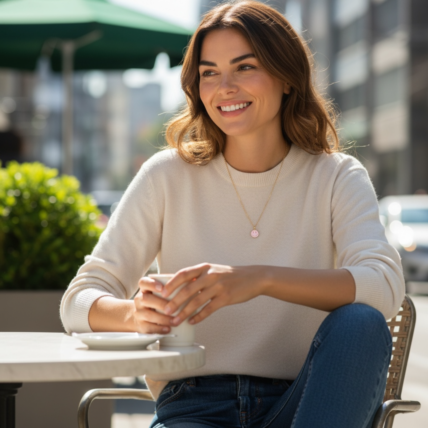 Woman wearing Dabble Doll charm and necklace, seated at a cafe with a sunny backdrop