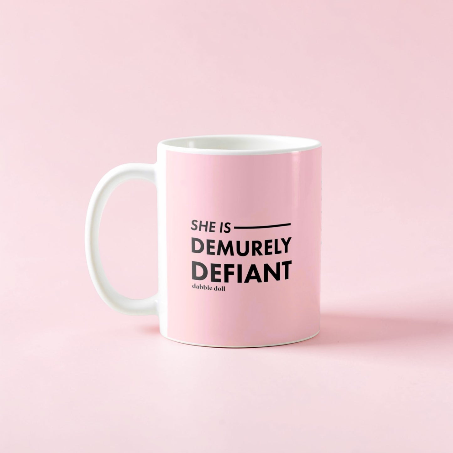 Dabble Doll coffee mug in pink with the phrase She Is Demurely Defiant printed on it