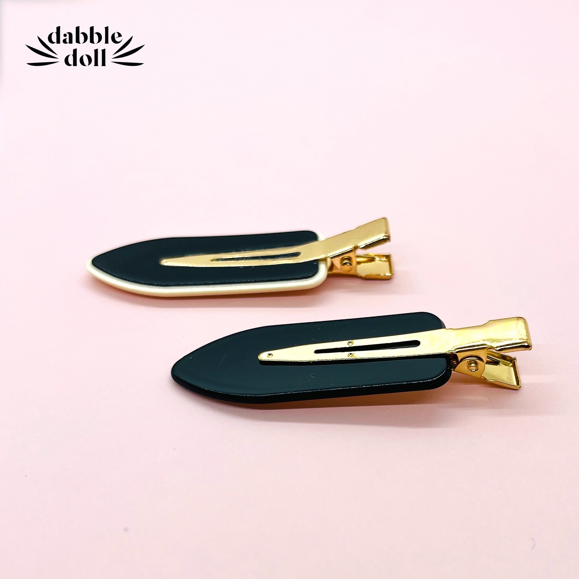 Dabble Doll black no bend hair clips with gold metal details on a pink background