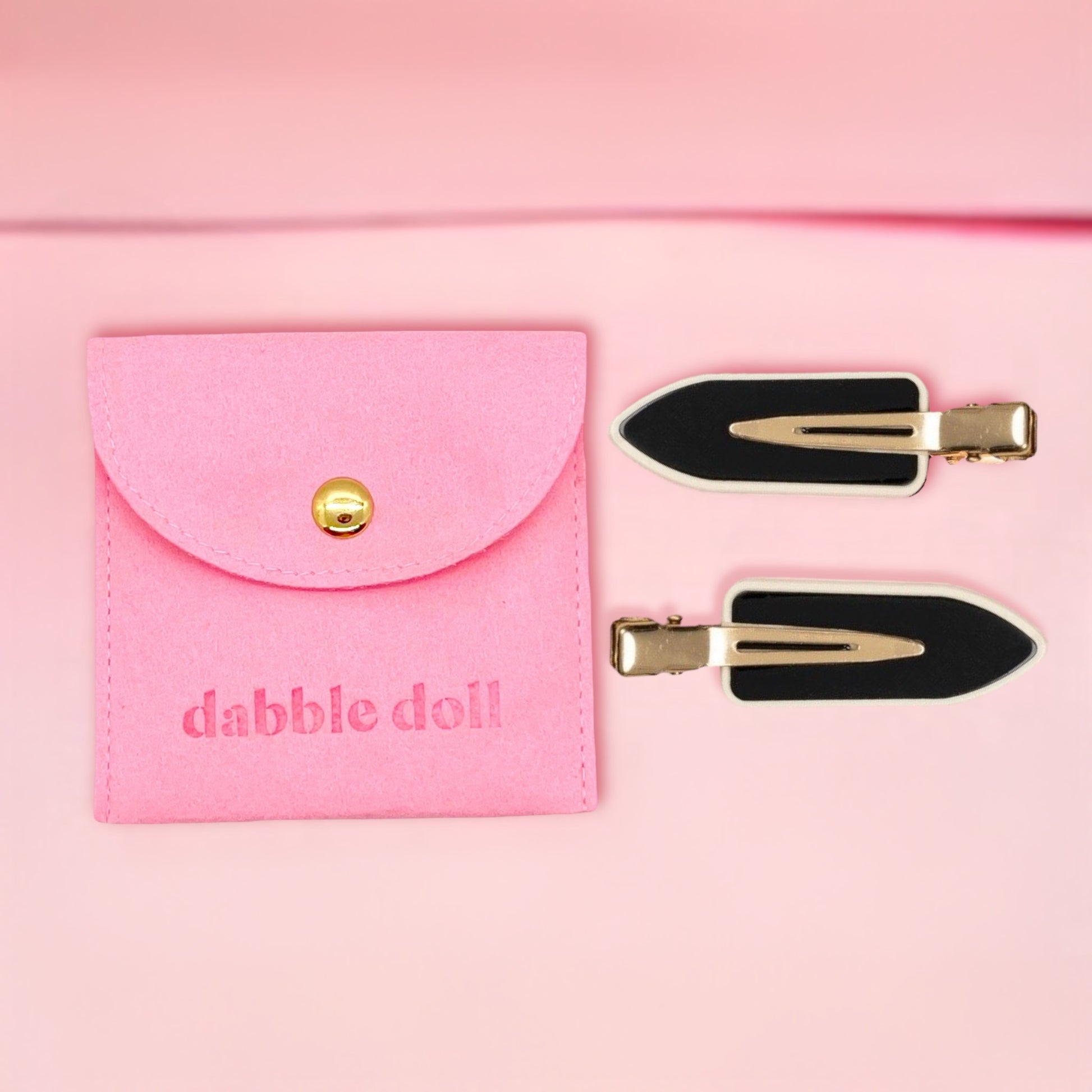 Dabble Doll black no bend hair clips with gold accents and pink storage pouch on light pink background