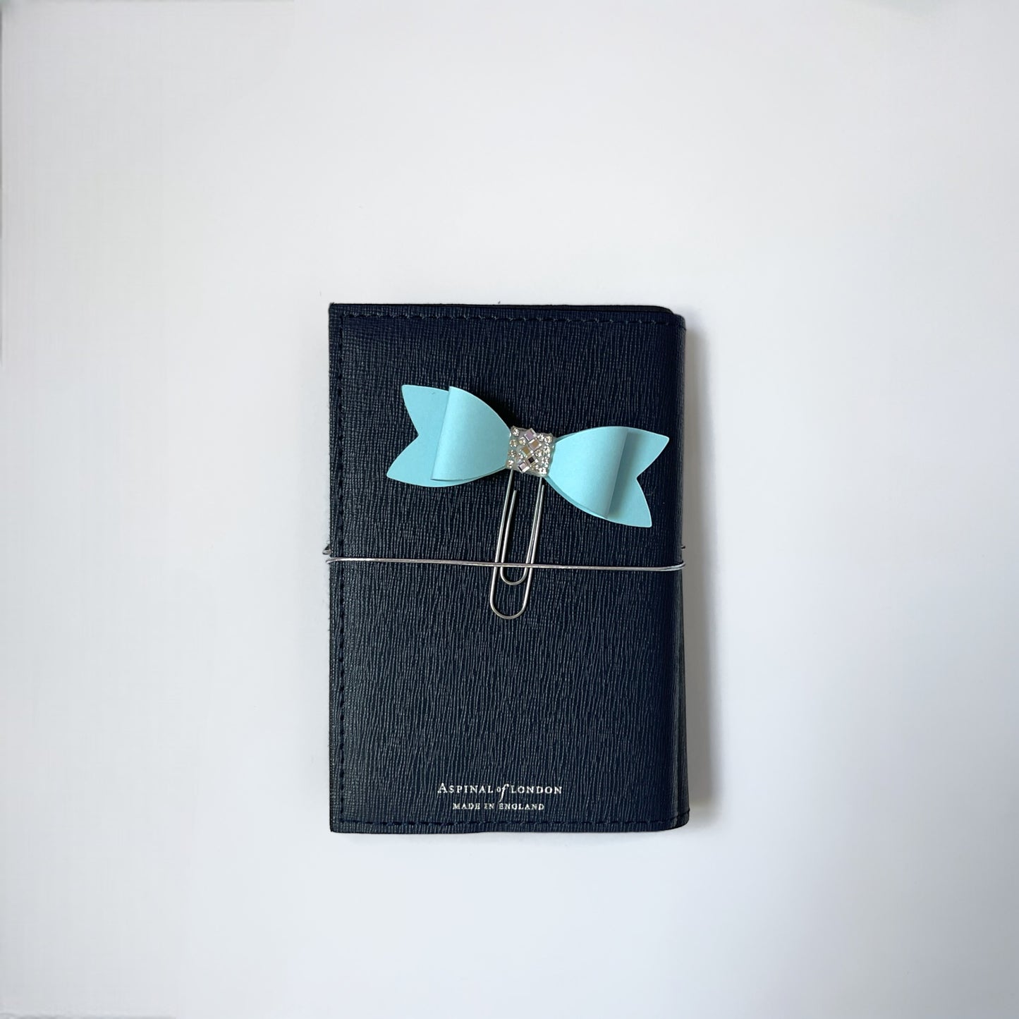 Dabble Doll Bow paperclip in light blue attached to a black notebook for stylish organization