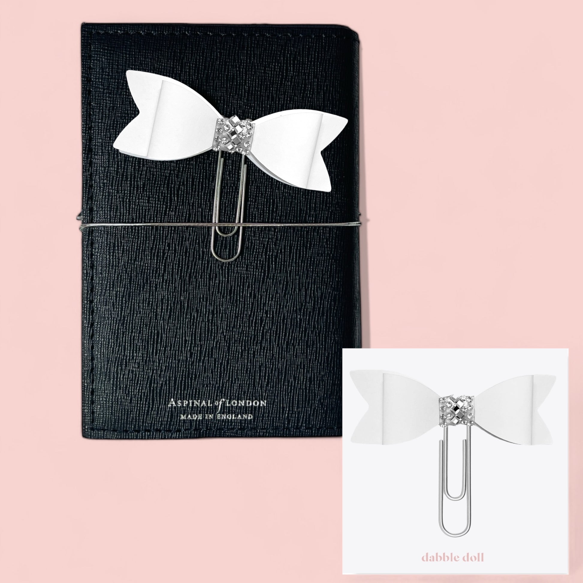 Dabble Doll Bow paperclip in white with rhinestone detail, accessorizing a black notebook