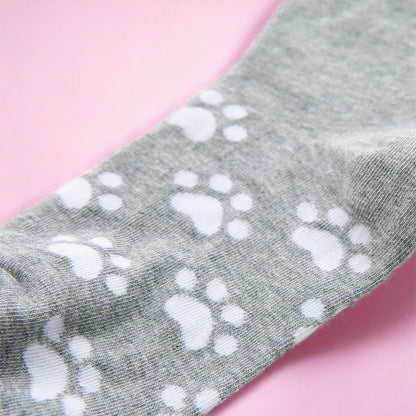 Gray sock with white paw prints from Dabble Doll cat socks gift box on pink background