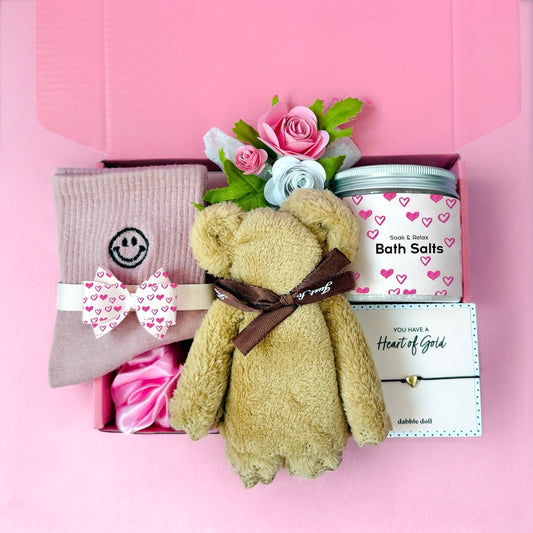Pink gift box for girls featuring teddy bear, bath salts, flowers, and cozy socks